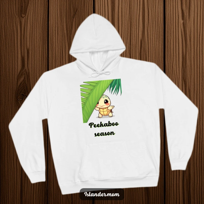 Funny curious turtle hoodie, featuring a turtle peeking from behind a palm leaf, offering warmth and a touch of island mystery.